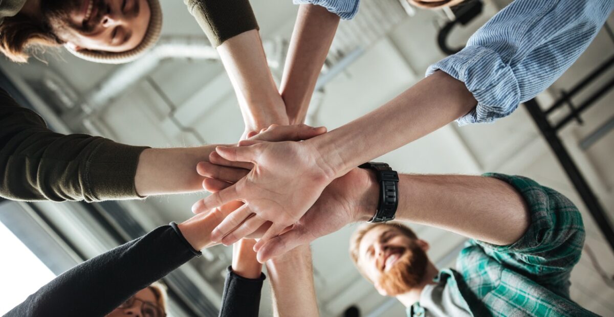 Image of young colleagues in office holding hands of each other. Looking aside.