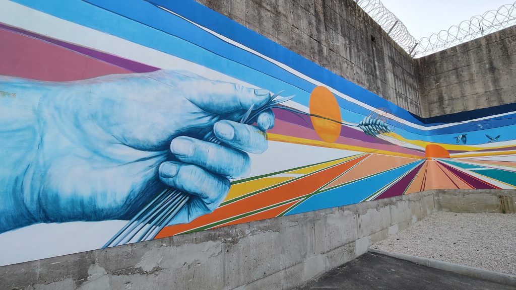 The ear of wheat in the mural at Pastificio Futuro - the grain that dies to generate new life, shared nourishment, and the possibility of rebirth.