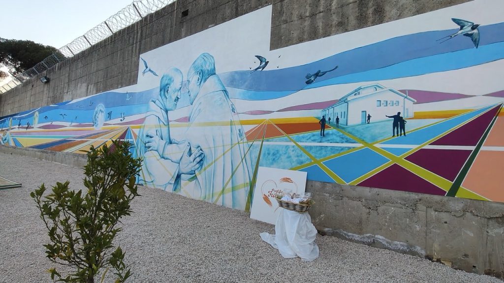The mural at Pastificio Futuro depicts the real embrace between Pope Francis and Father Gaetano Greco, chaplain of the Casal del Marmo juvenile prison, where the project began.